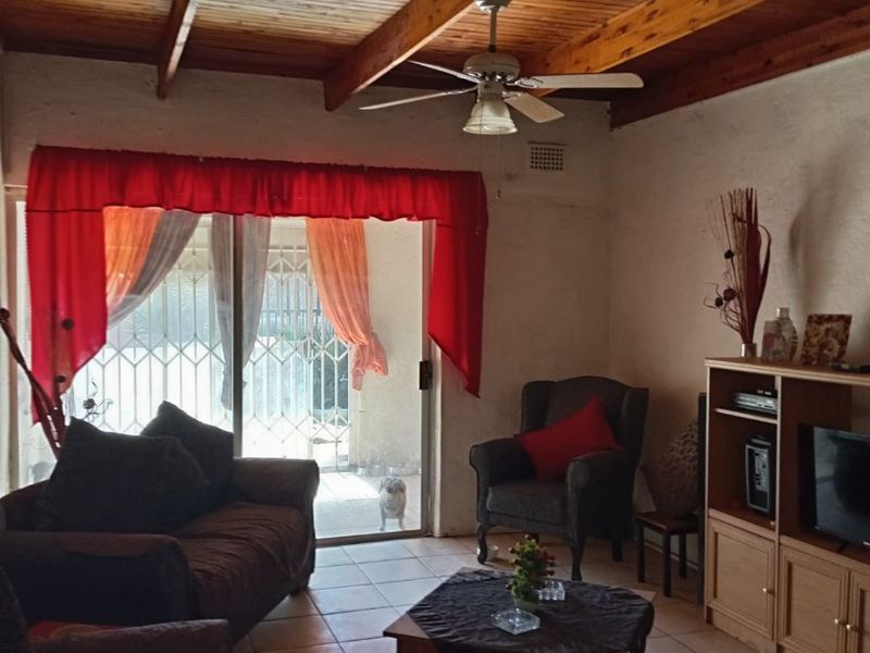 A living room featuring a rustic exposed timber beam ceiling, tiled flooring, and a sliding glass door providing access to the exterior.