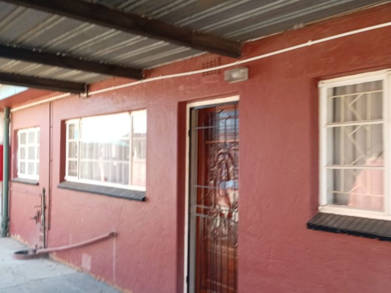 A covered outdoor patio area featuring a corrugated metal roof, security gate, and security bars on the windows.