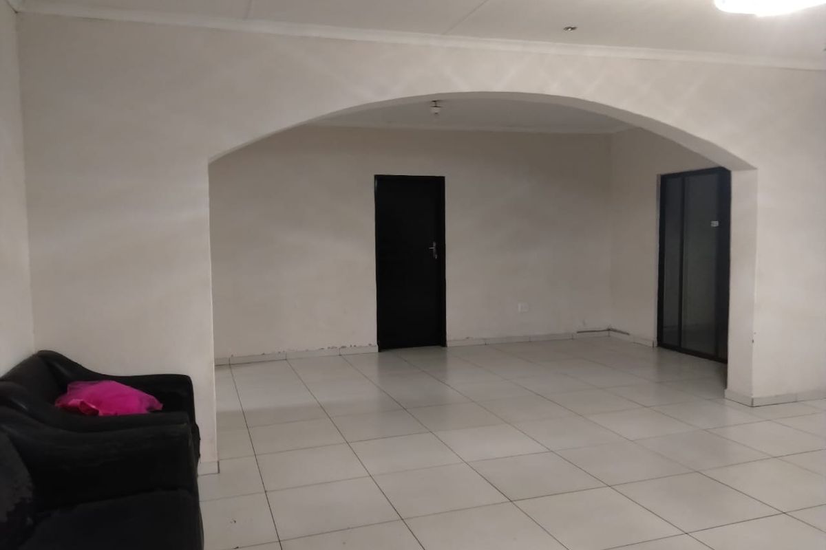 A spacious, open-plan living area featuring neutral tiled flooring, recessed lighting, and a distinctive arched architectural detail connecting to adjacent spaces.