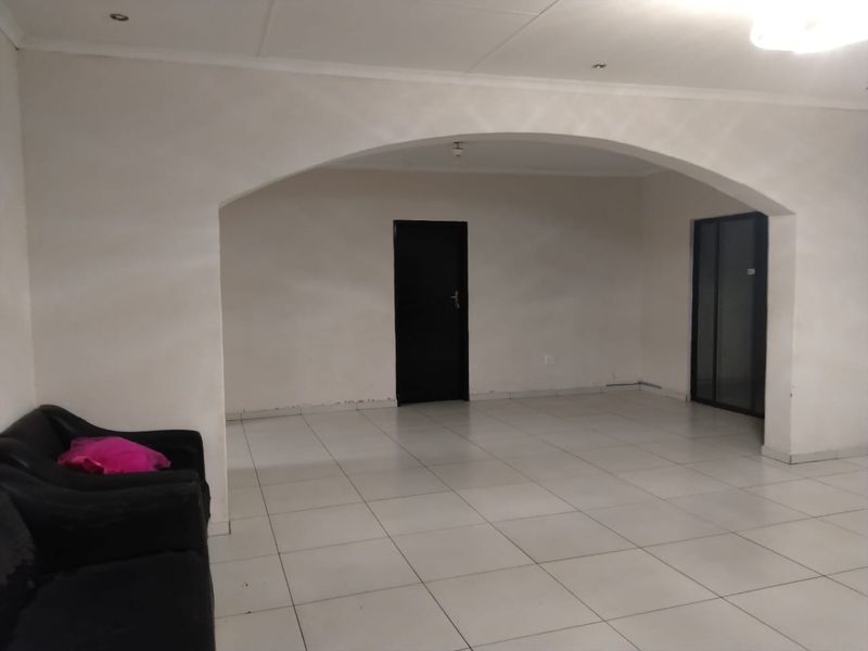 A spacious, open-plan living area featuring neutral tiled flooring, recessed lighting, and a distinctive arched architectural detail connecting to adjacent spaces.