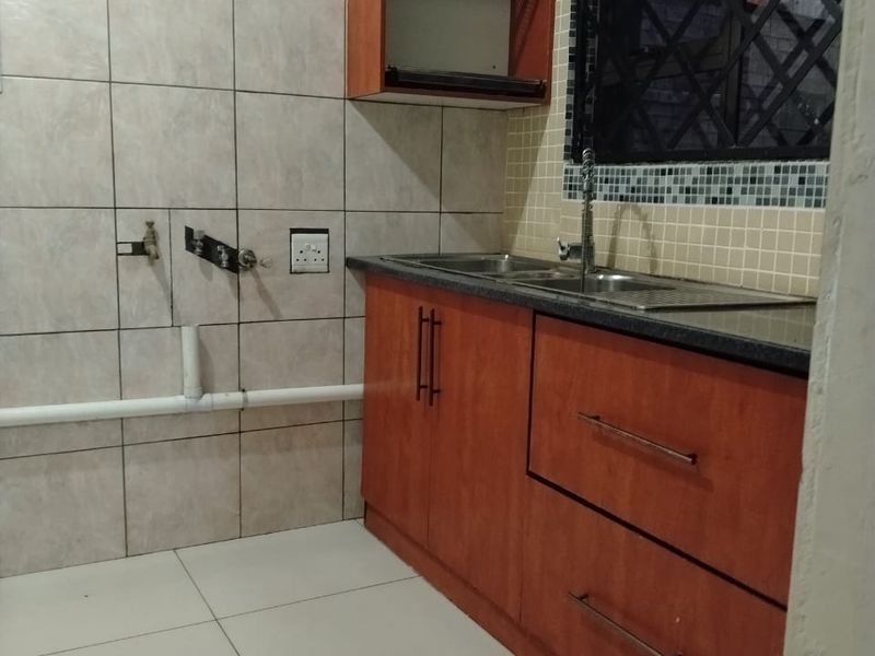 A functional scullery area featuring built-in wooden cabinetry, a stainless steel sink, and tiled wall finishes with dedicated plumbing connections for appliances.