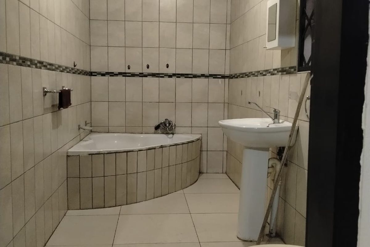 A dated bathroom featuring a corner bathtub, pedestal basin, and toilet with full-height wall tiling.