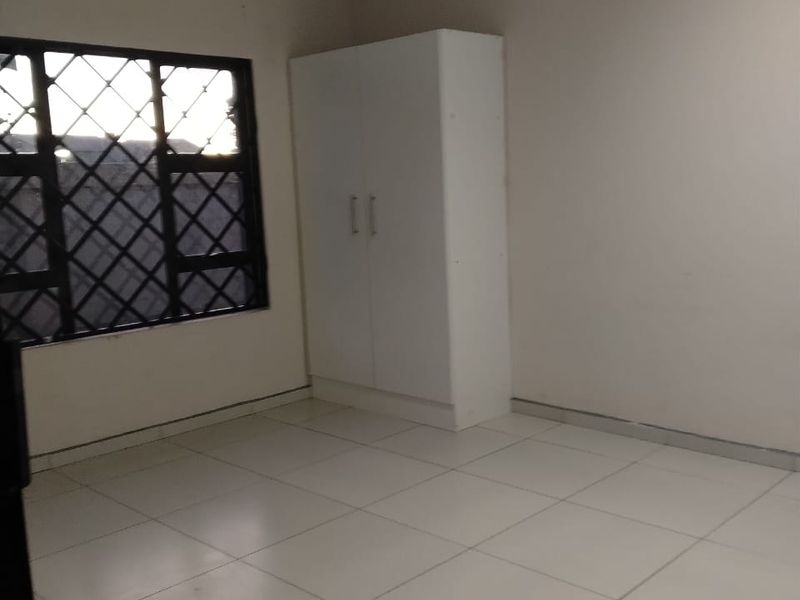 A clean, empty bedroom featuring neutral tiled flooring, a built-in wardrobe, and windows fitted with security bars.