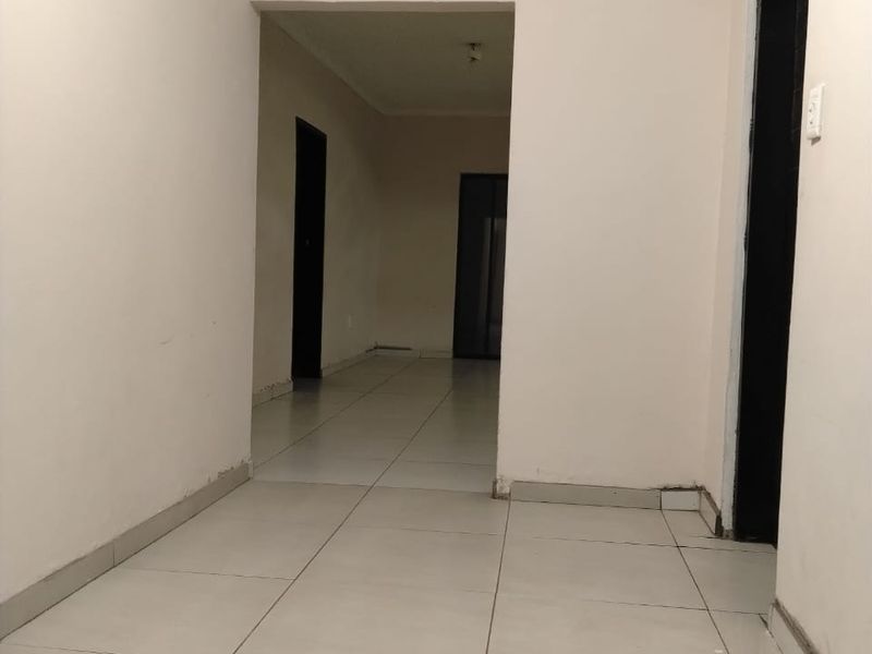 A vacant interior hallway featuring neutral tiled flooring and plain walls, providing access to multiple rooms within the property.
