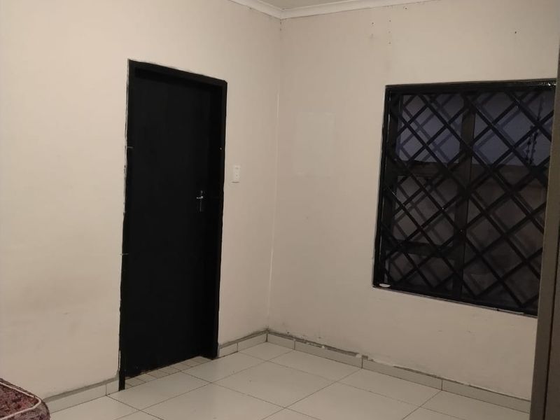 A simple, empty bedroom featuring tiled flooring, a window with security bars, and a neutral color palette, ready for personalization.
