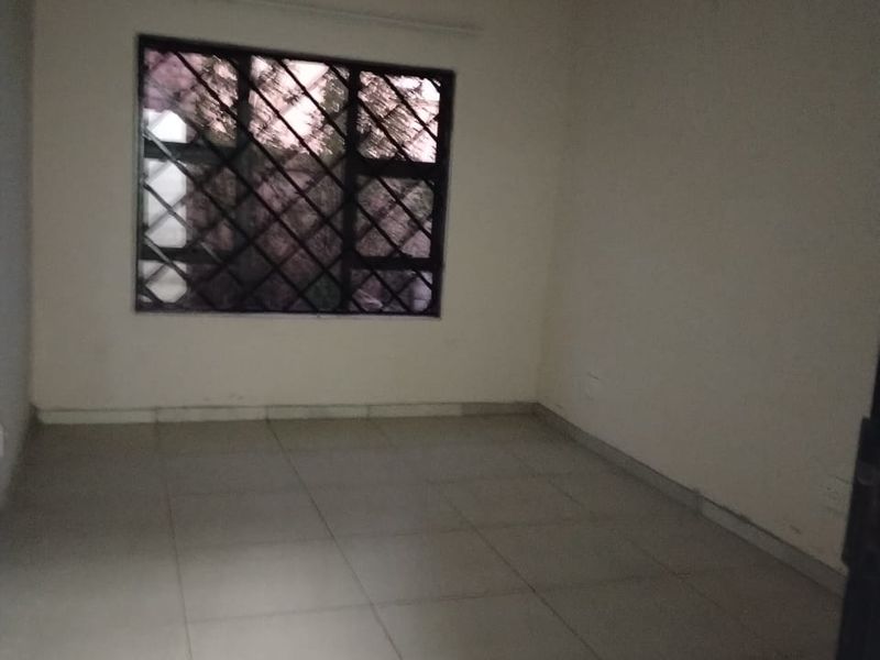 An empty bedroom featuring neutral tiled flooring and a window fitted with security burglar bars.