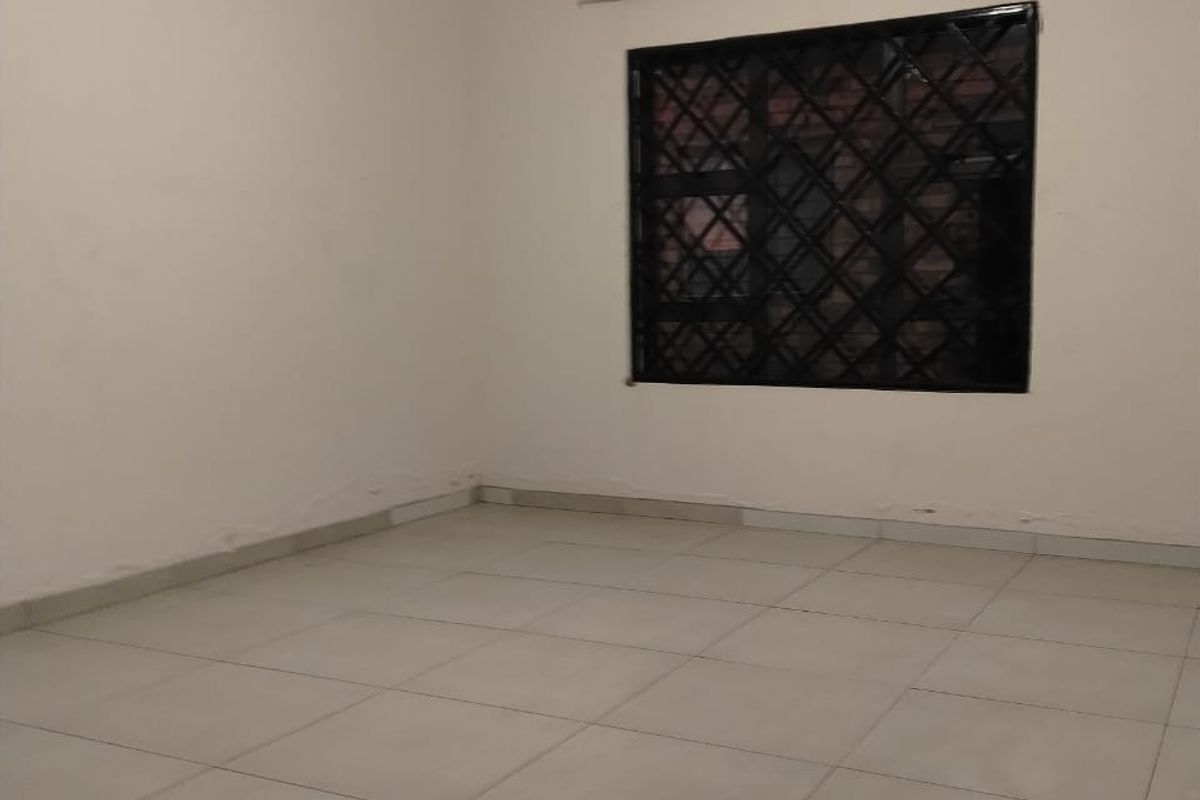 A clean, empty bedroom featuring neutral tiled flooring and a window fitted with security bars.