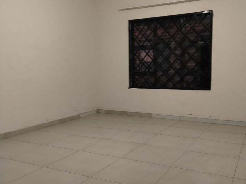 A clean, empty bedroom featuring neutral tiled flooring and a window fitted with security bars.