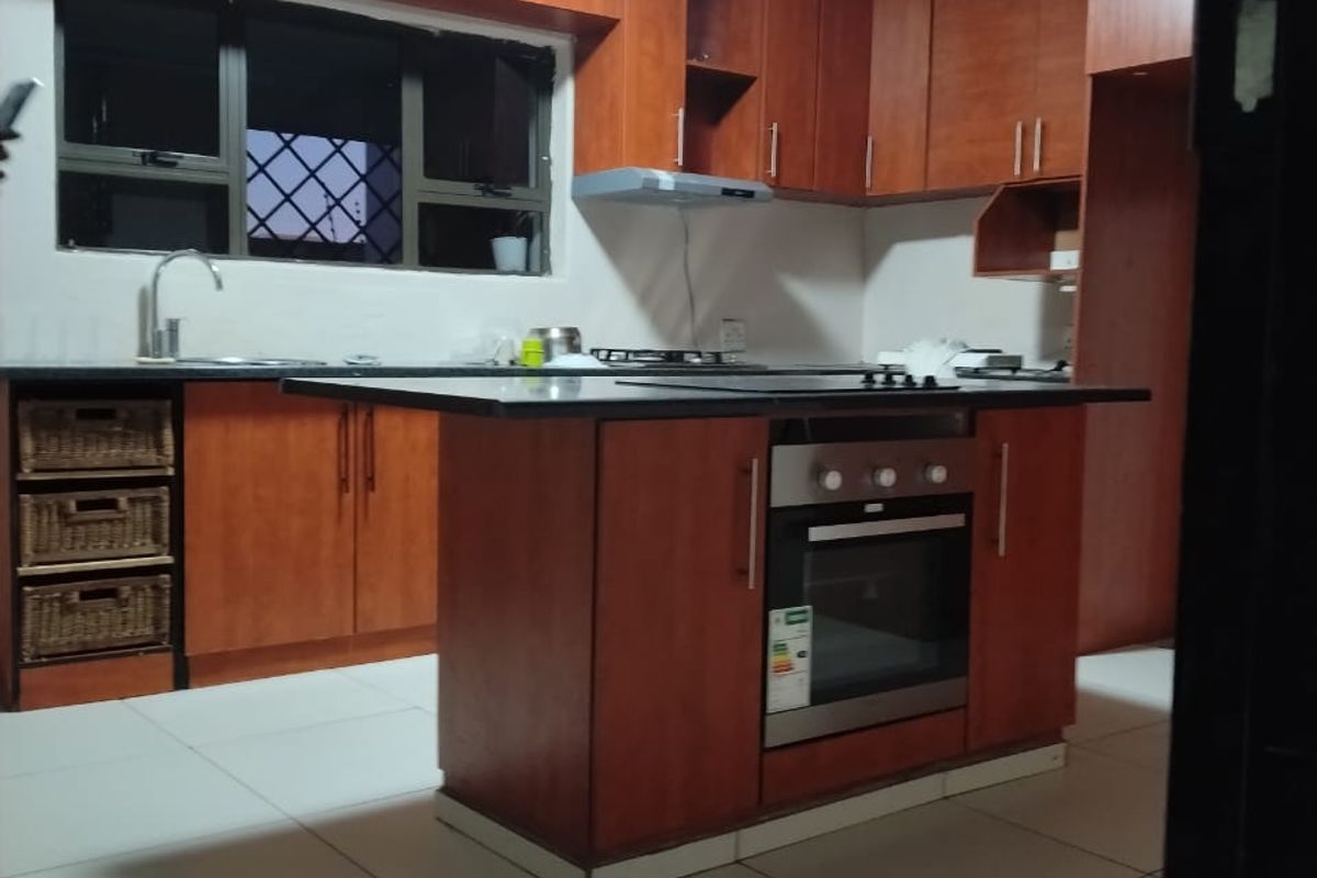 A functional kitchen featuring wood-finish cabinetry, a central island with a built-in oven and hob, and tiled flooring.