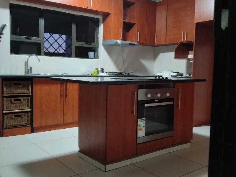 A functional kitchen featuring wood-finish cabinetry, a central island with a built-in oven and hob, and tiled flooring.