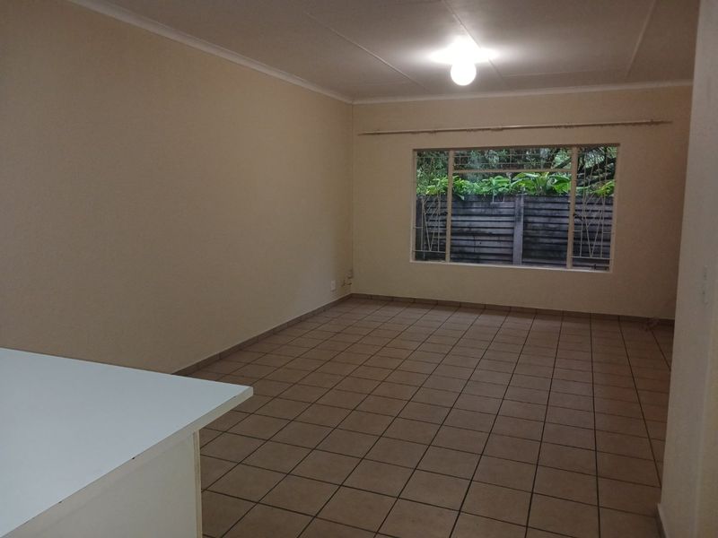 An empty open-plan living area featuring tiled flooring, a large window with security bars, and a neutral color palette.