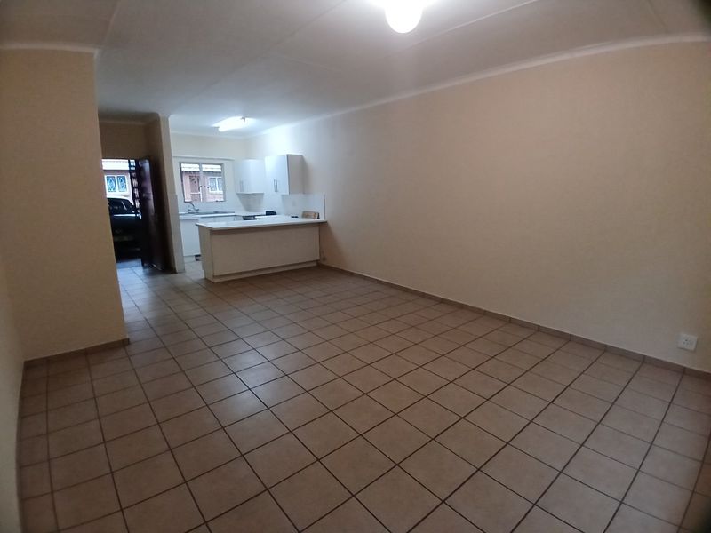 An open-plan living and kitchen area featuring neutral tiled flooring, white cabinetry, and a breakfast bar, offering a clean and versatile living space.