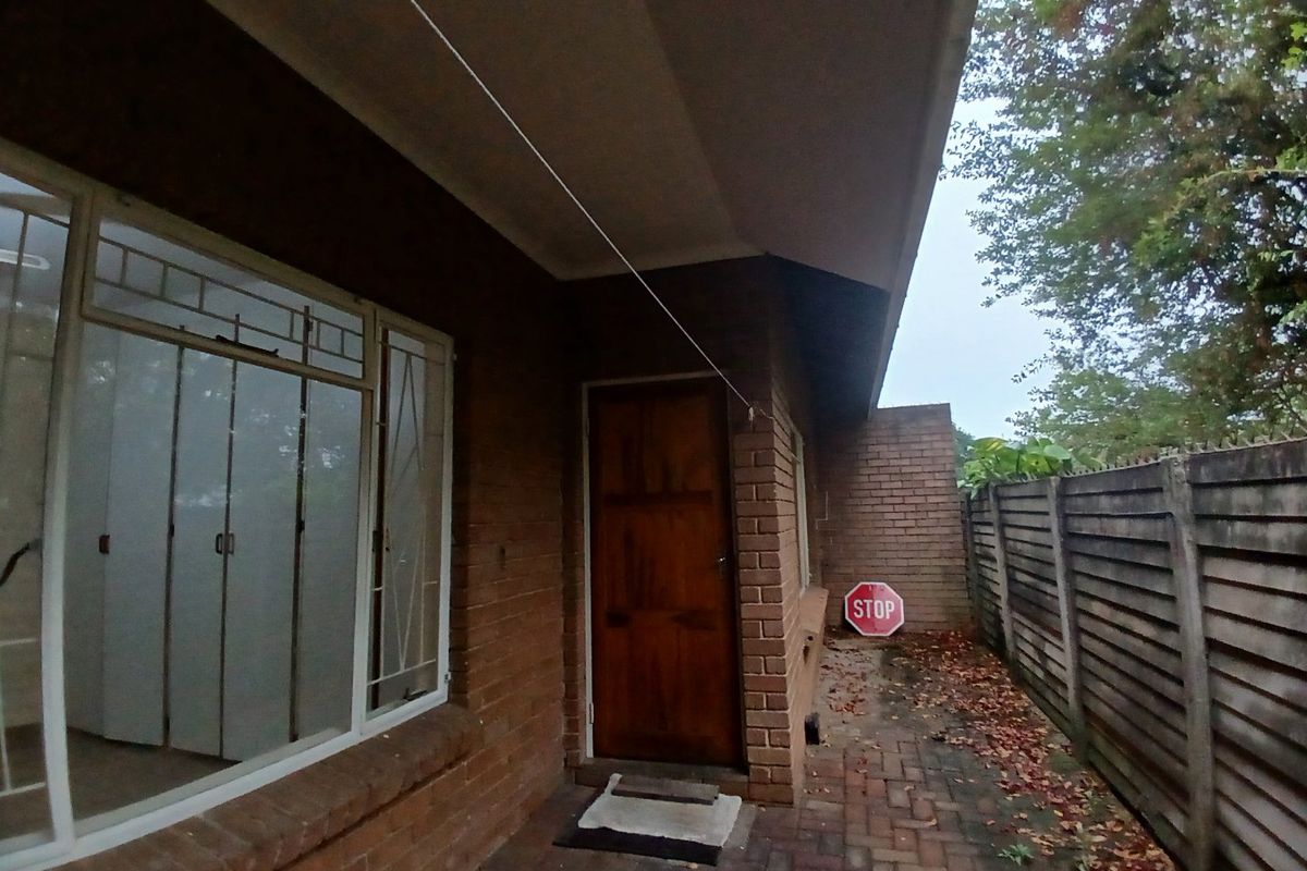 Rear exterior view of the property featuring brick paving, a timber door, and a precast concrete boundary wall.