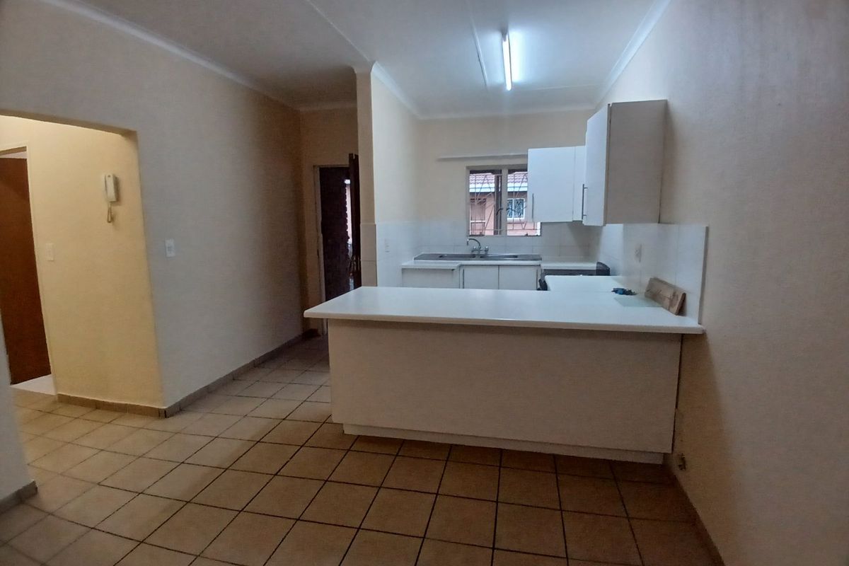 A functional, empty kitchen featuring white cabinetry, a central island, tiled flooring, and a double sink, offering a clean canvas for updates.