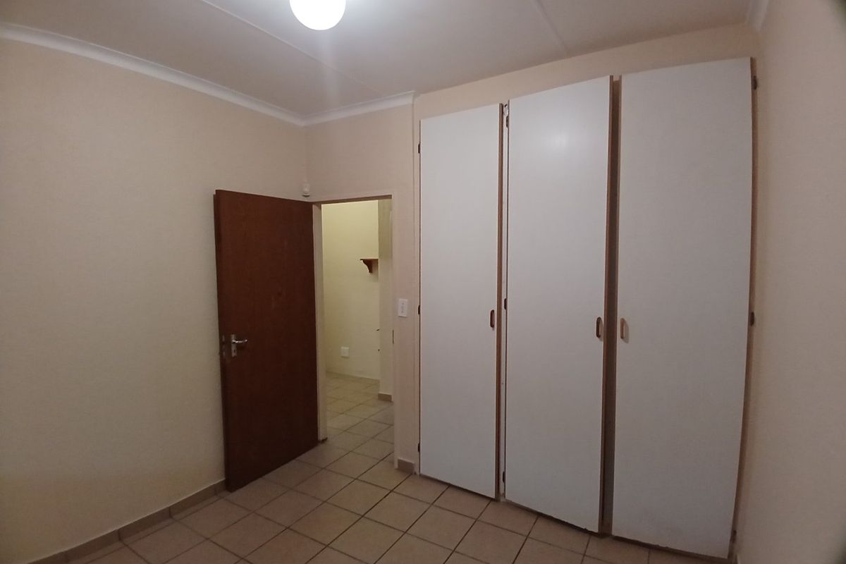 A clean, empty bedroom featuring neutral tiled flooring, built-in white cupboards, and a simple interior door leading to an adjacent space.