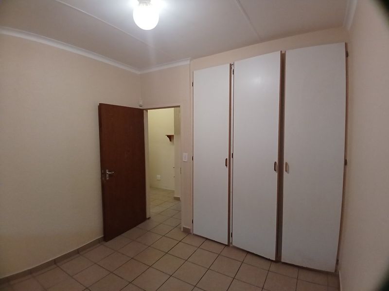 A clean, empty bedroom featuring neutral tiled flooring, built-in white cupboards, and a simple interior door leading to an adjacent space.