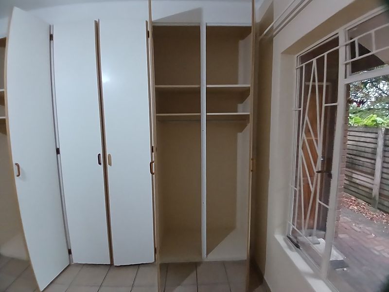 A bedroom featuring built-in cupboards, tiled flooring, and a window with a security gate, offering a clean and functional space.