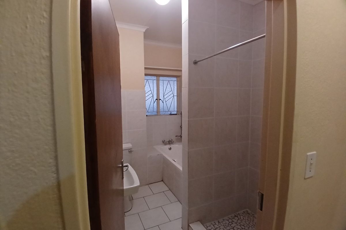 A functional bathroom featuring a separate bathtub and shower cubicle with tiled finishes and a window for natural light.
