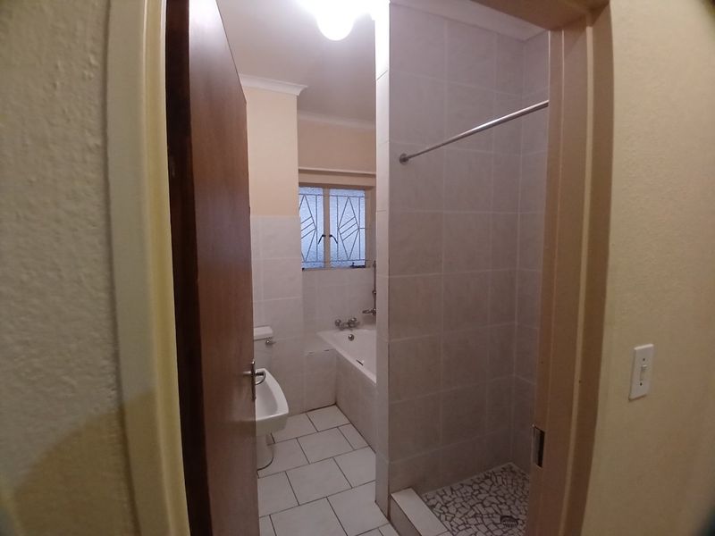 A functional bathroom featuring a separate bathtub and shower cubicle with tiled finishes and a window for natural light.