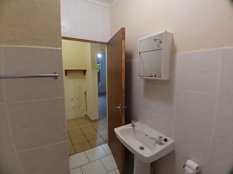 A functional bathroom featuring a pedestal basin, wall-mounted medicine cabinet, and neutral tiled finishes, leading into an adjacent utility or laundry area.
