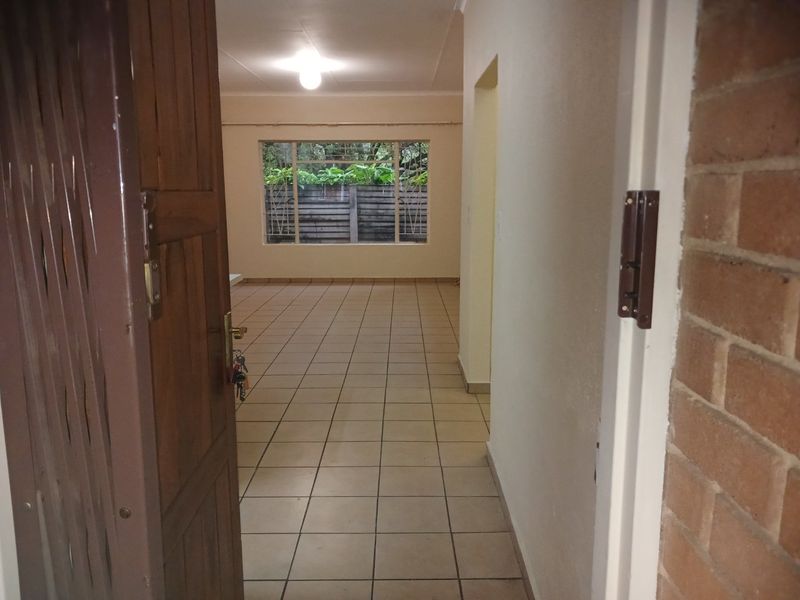 Entrance area leading into an open-plan living space with tiled flooring, exposed brick accents, and natural light through a large window.