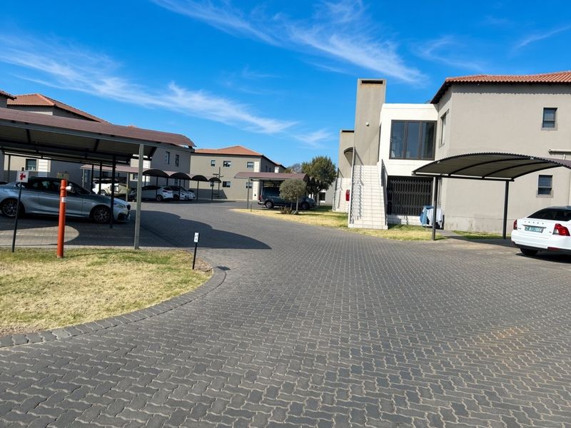 Exterior view of an apartment complex featuring paved driveways, covered parking carports, and multi-story residential units with external staircases.