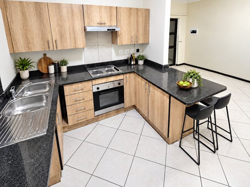 Modern kitchen featuring light wood-finish cabinetry, dark granite countertops, stainless steel appliances, and neutral ceramic floor tiles in an open-plan layout.