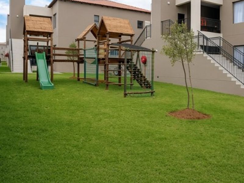 A well-maintained communal garden area featuring a children's play structure, manicured lawn, and access to apartment building balconies.