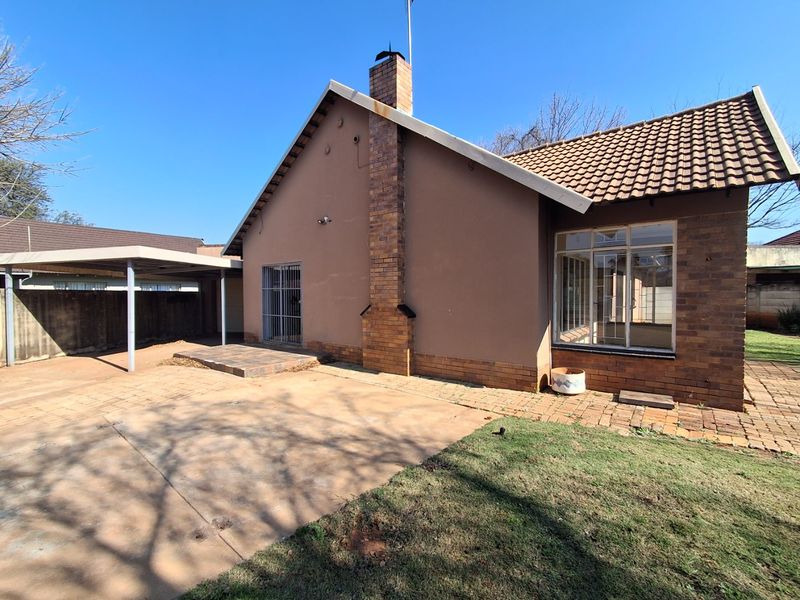 Rear view of the house featuring a brick chimney, paved patio area, and an attached carport structure.