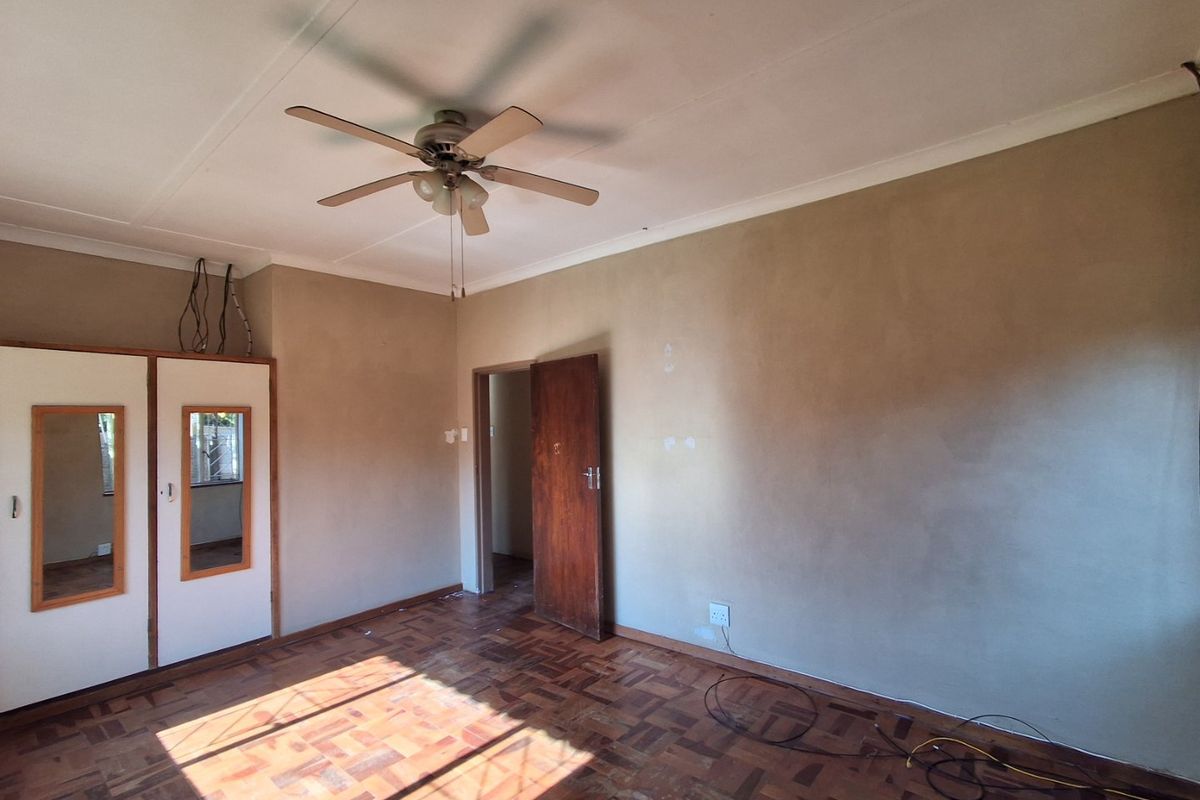 An empty bedroom featuring original parquet flooring, built-in cupboards, and a ceiling fan, requiring cosmetic updates to the walls and electrical finishes.