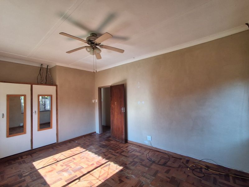 An empty bedroom featuring original parquet flooring, built-in cupboards, and a ceiling fan, requiring cosmetic updates to the walls and electrical finishes.