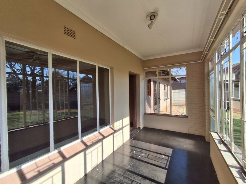 A covered, enclosed patio area featuring large glass windows, painted brick walls, and concrete flooring, offering a bright and versatile outdoor living space.