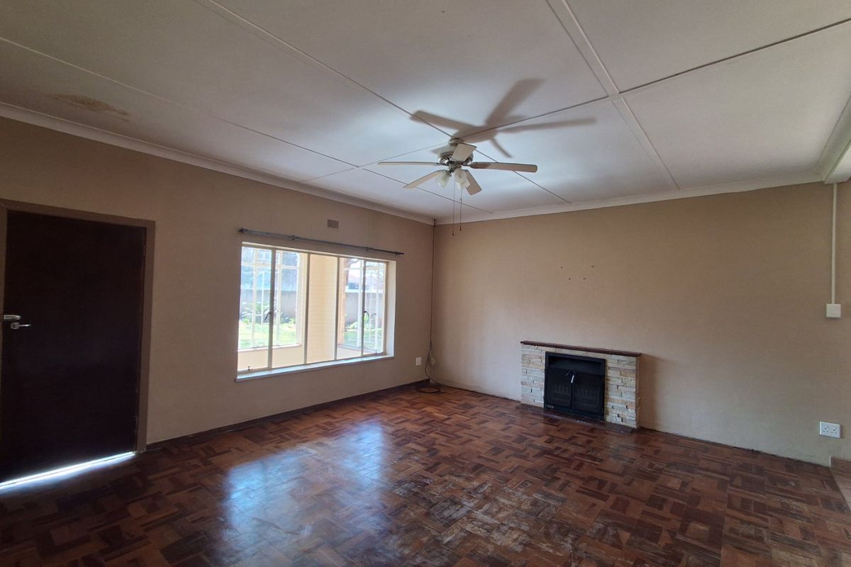 Spacious living room featuring original parquet flooring, a built-in fireplace with stone detailing, and a ceiling fan, offering a blank canvas for renovation.