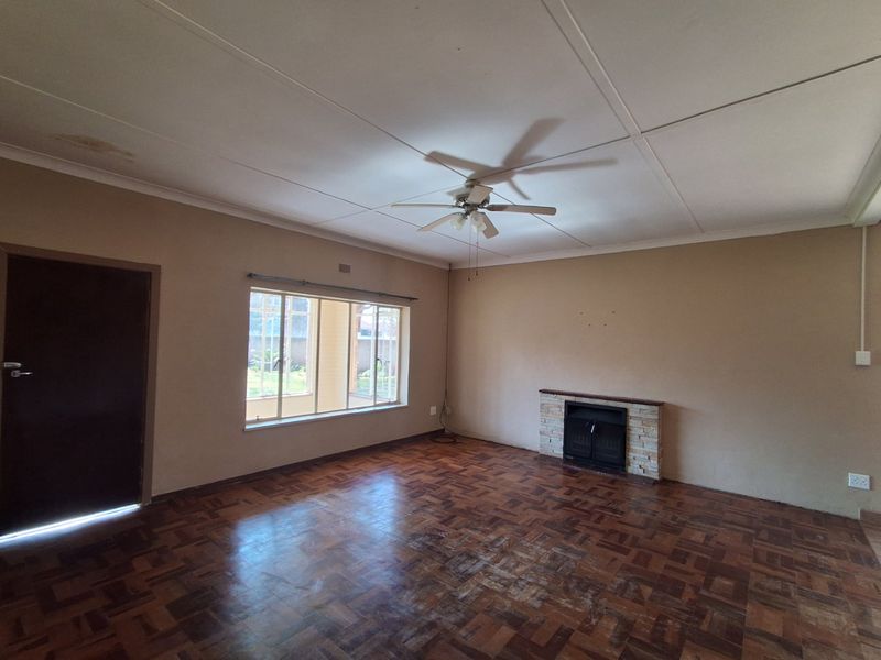 Spacious living room featuring original parquet flooring, a built-in fireplace with stone detailing, and a ceiling fan, offering a blank canvas for renovation.