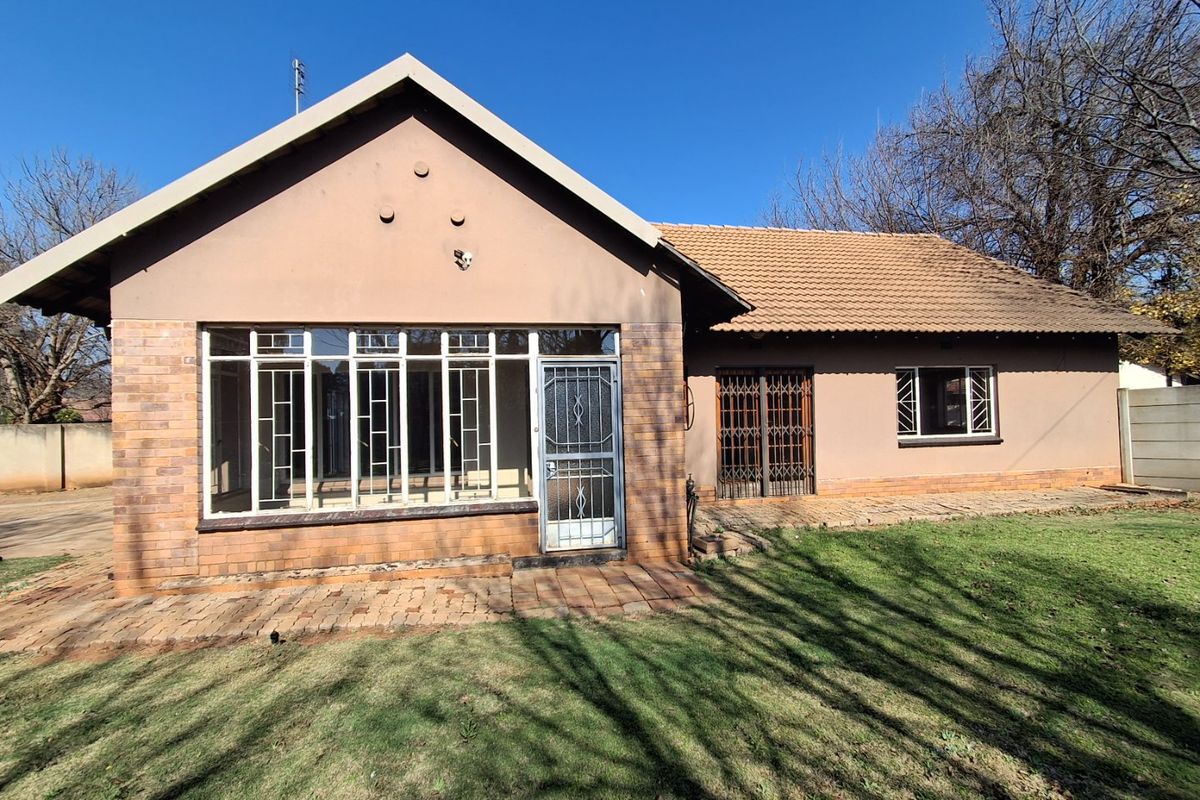 Rear view of a single-story house featuring a brick facade, tiled roof, security gates, and a paved patio area overlooking the garden.
