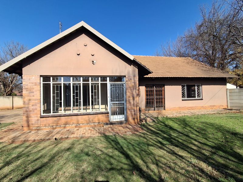 Rear view of a single-story house featuring a brick facade, tiled roof, security gates, and a paved patio area overlooking the garden.