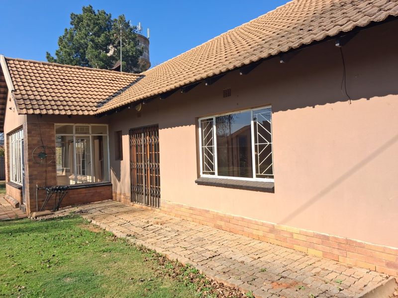 Rear view of the house featuring a tiled roof, brick and plastered facade, security gate, and a paved walkway leading along the exterior.