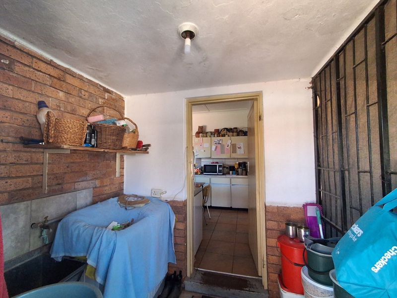 A functional scullery area featuring a utility sink, exposed brick wall, and direct access to the kitchen, showing signs of wear.