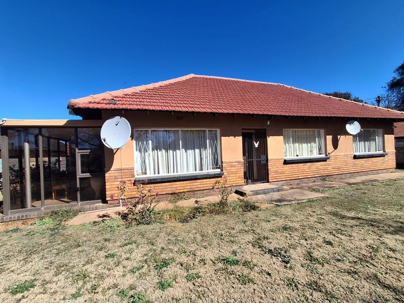 Rear view of a single-story brick house featuring a tiled roof, security gates, and an enclosed patio area set within a garden.