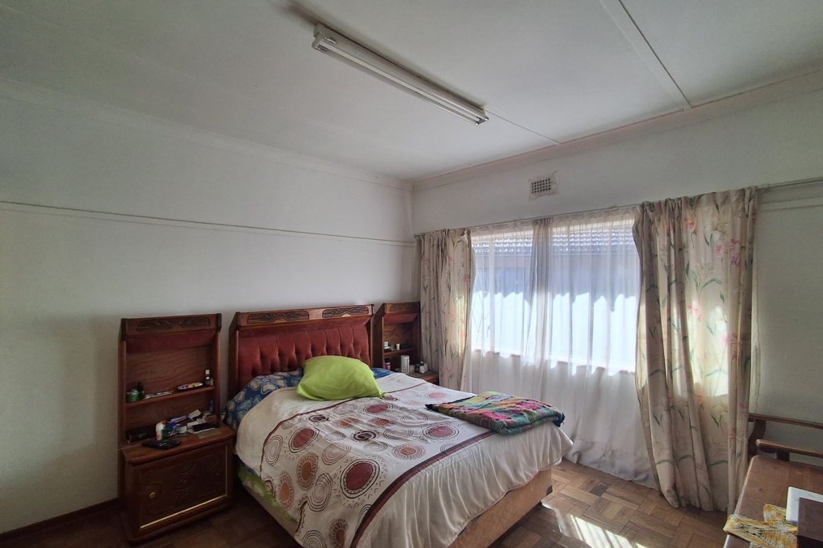 A bedroom featuring original parquet flooring, a large window with curtains, and a functional ceiling light fixture.