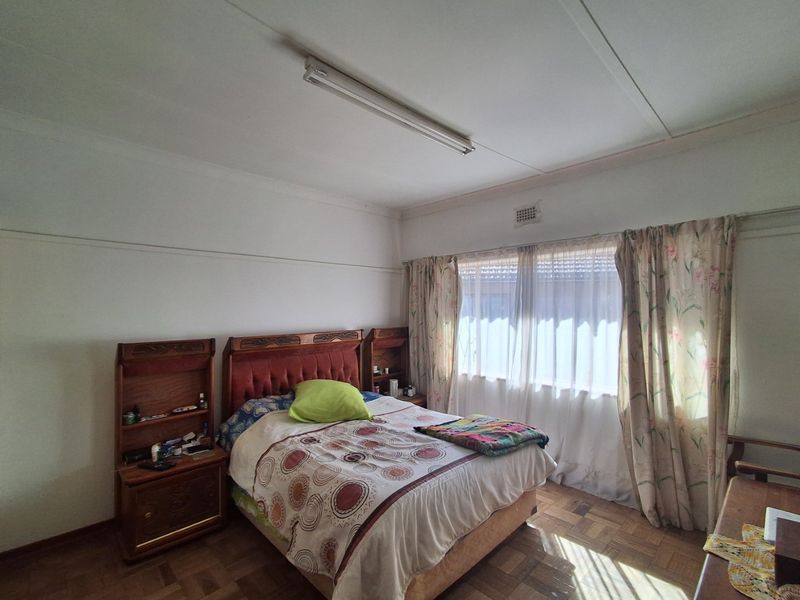 A bedroom featuring original parquet flooring, a large window with curtains, and a functional ceiling light fixture.