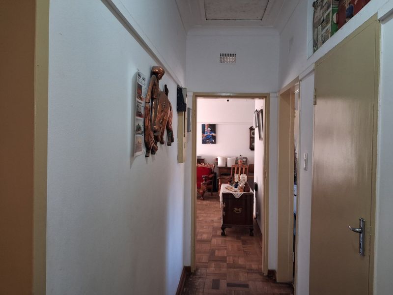 A narrow residential hallway featuring parquet flooring and access to adjacent rooms, showing signs of wear and dated finishes.