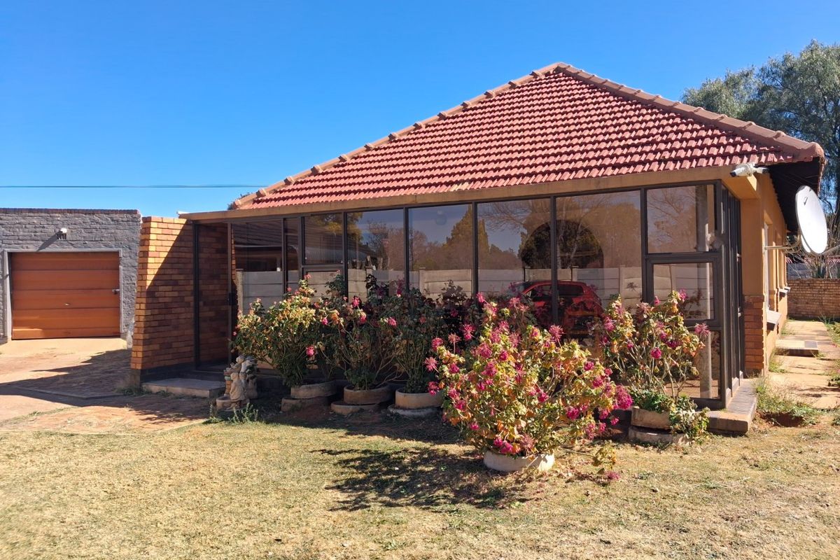 Rear view of the property featuring an enclosed patio area, tiled roof, and a separate garage with a paved driveway.