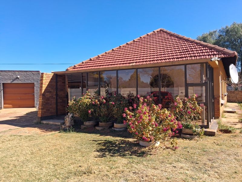 Rear view of the property featuring an enclosed patio area, tiled roof, and a separate garage with a paved driveway.