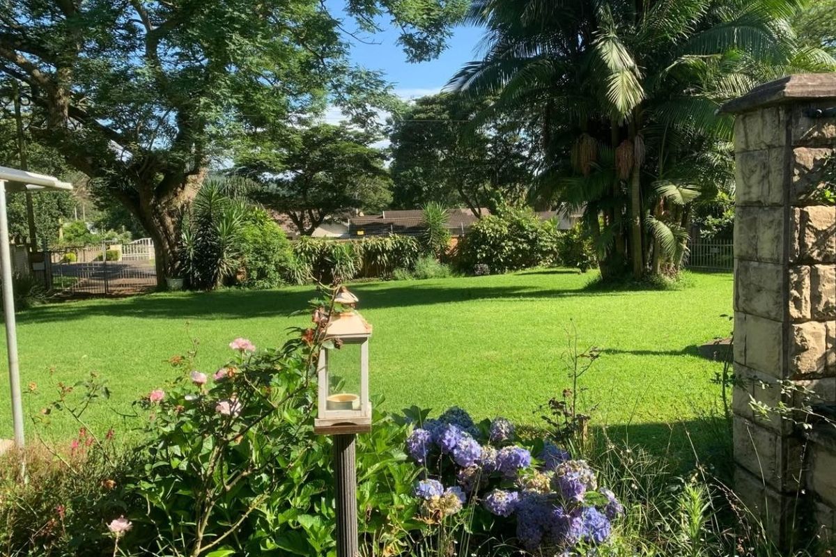 A well-maintained, lush green garden featuring mature trees, established landscaping, and a stone pillar boundary element.