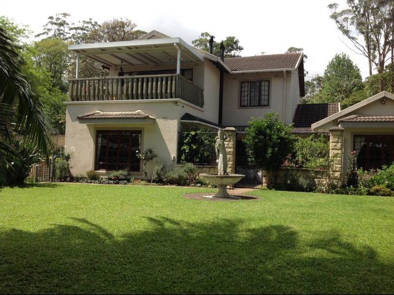 Rear view of a two-story residence featuring a covered balcony, stone accents, and a well-maintained garden with a central fountain.
