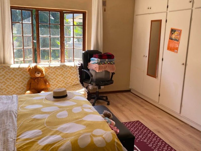 A bedroom featuring built-in cupboards, a ceiling fan, and timber-framed windows, offering a functional space with potential for cosmetic updates.
