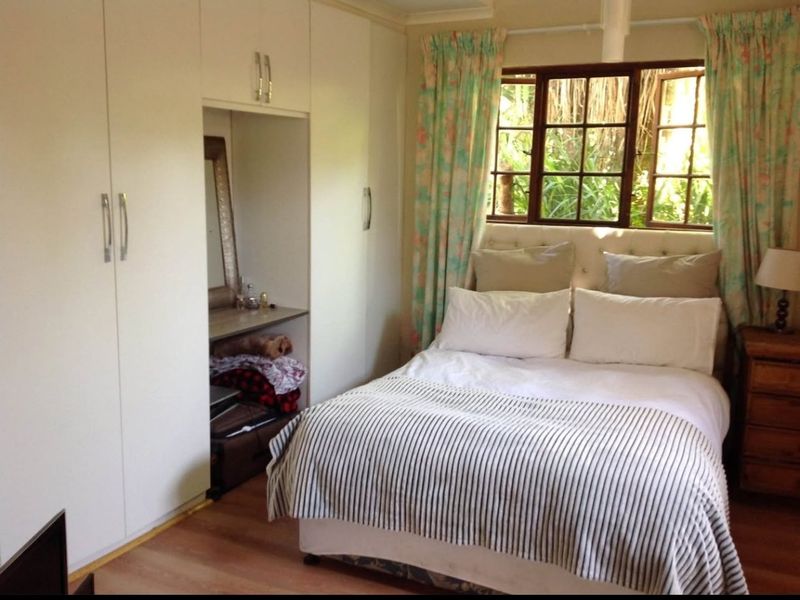 A cozy bedroom featuring built-in cupboards, laminate flooring, and timber-framed windows overlooking a garden area.