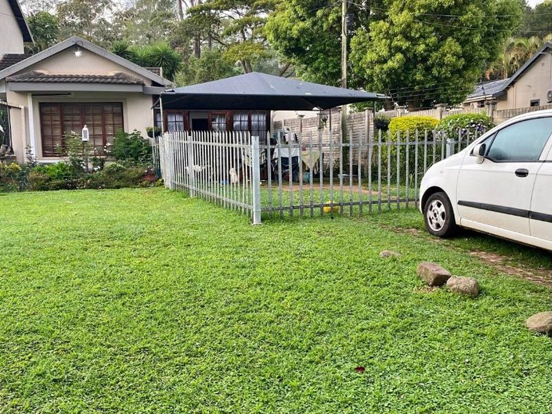 Front view of a residential property featuring a lawn, paved driveway, metal perimeter fencing, and a tiled roof structure.