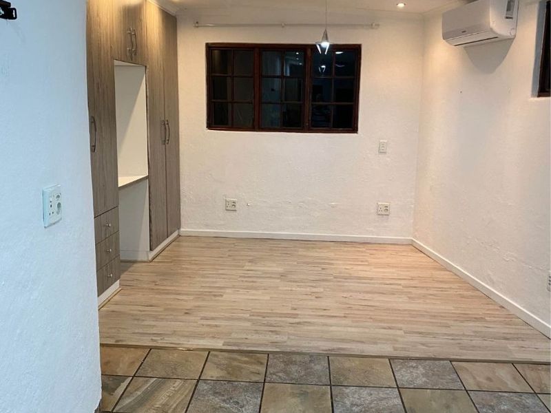 An empty living area featuring a combination of tiled and laminate flooring, built-in cabinetry, and a wall-mounted air conditioning unit.